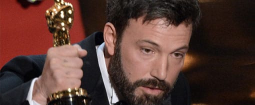 Ben Affleck, holding an Oscar trophy and speaking into a microphone at an awards ceremony.