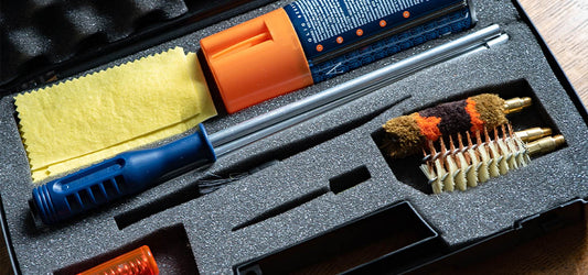 Gun cleaning kit with brushes, rods, and cloths in a foam-padded case.