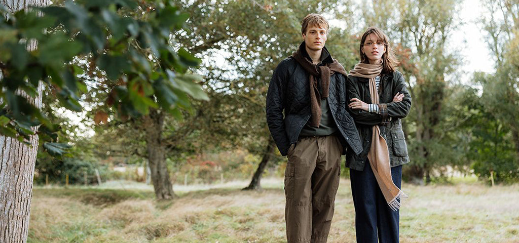 Young couple in casual outdoor jackets and scarves standing in a leafy park, reflecting a relaxed autumn style.