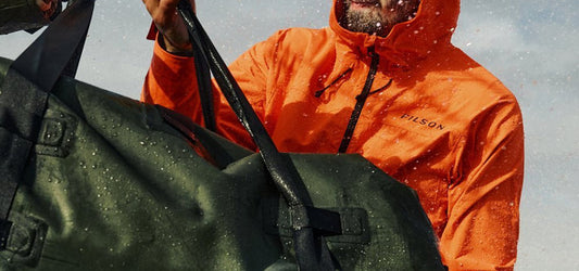 Person in an orange Filson jacket carrying a wet Filson bag