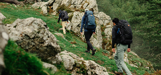 Three hikers wearing Fjallraven backpacks trekking through a rocky, moss-covered hillside.