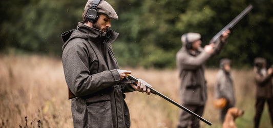 A group of hunters in a field, one in focus holding a shotgun, with others in the background aiming their firearms.