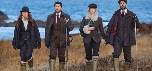 Four people in elegant outdoor clothing and Le Chameau boots walking along a coastal path.