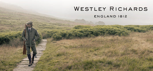 A man dressed in traditional shooting attire carrying a shotgun and walking along a path in the countryside, with the text "Westley Richards England 1812" above.